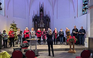 Chormitglieder stehen im Halbkreis in einer Kirche. Davor steht die Chorleiterin.
