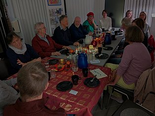 13 Menschen sitzen um einen adventlich geschmückten Tisch