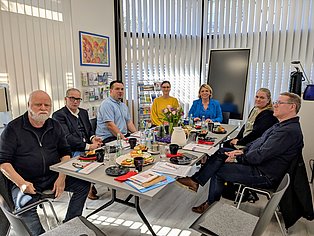 Vier Männer und eine Frau sitzen um einen großen Tisch im Gruppenraum des Selbsthilfe-Büros