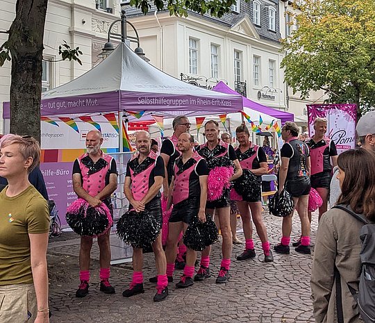 Eine Gruppe Männer als Cheerleader stellen sich vor dem Infostand auf